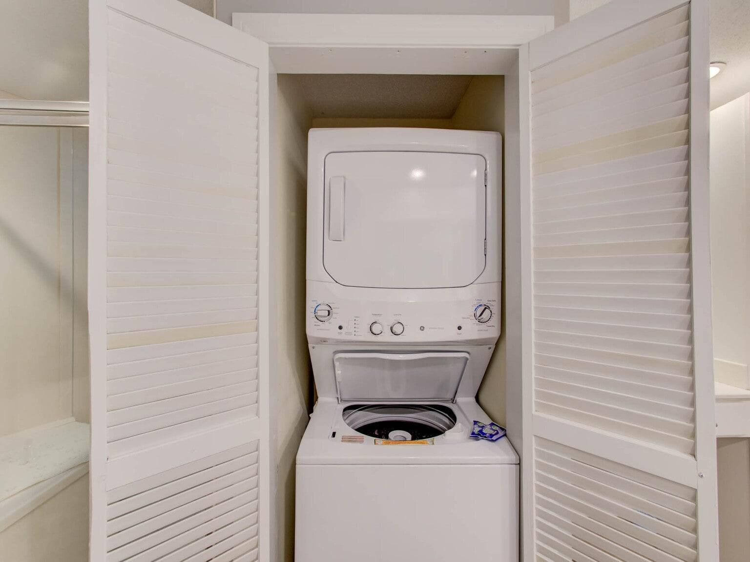 A compact, white laundry room with a built-in washer and dryer, enclosed by white paneling.