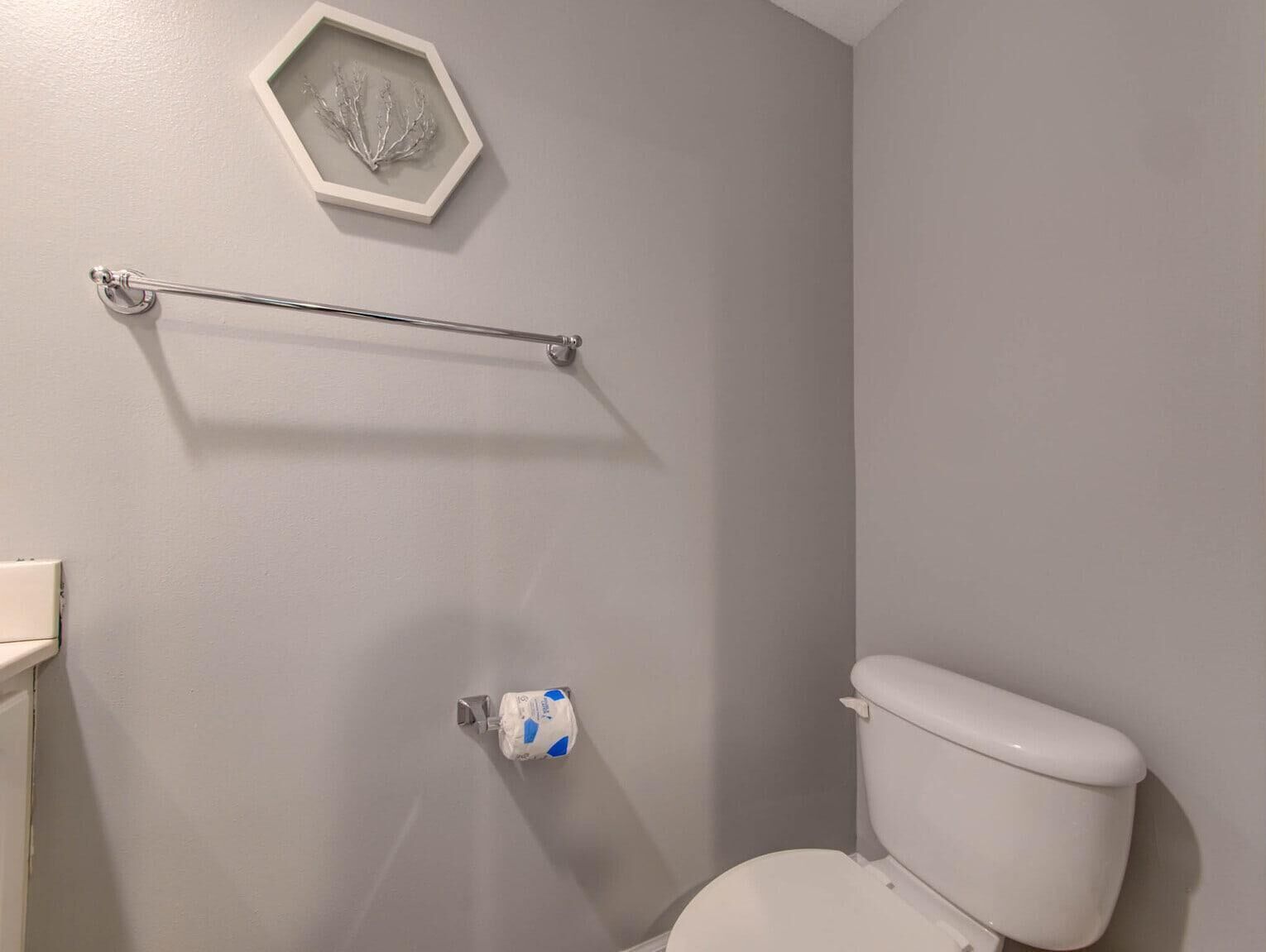 Un baño con inodoro, toallero y un adorno en la pared enmarcado.