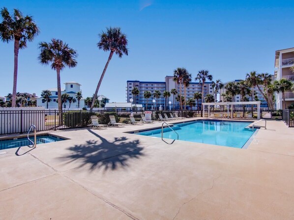 A pool area with lounge chairs, palm trees, and a building in the background.