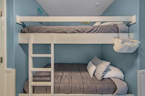 A bunk bed with a ladder, a white shelf above, and a white basket hanging on the wall.