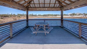 Una terraza cubierta de madera con una mesa de picnic, un letrero que dice 'NO FISHING' y vistas a un cuerpo de agua y edificios lejanos.