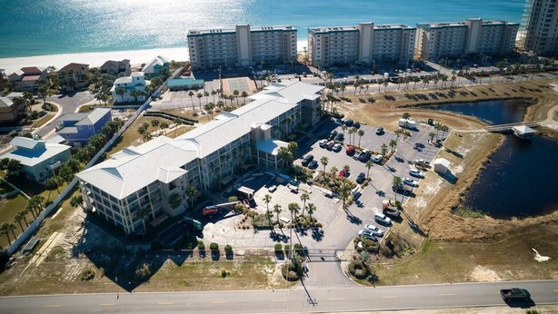 Vista aérea de un complejo hotelero con varias construcciones, un estacionamiento y una playa al fondo.