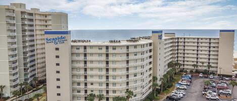 A multi-story hotel with a beach and racquet club sign, parking lot, and ocean view.