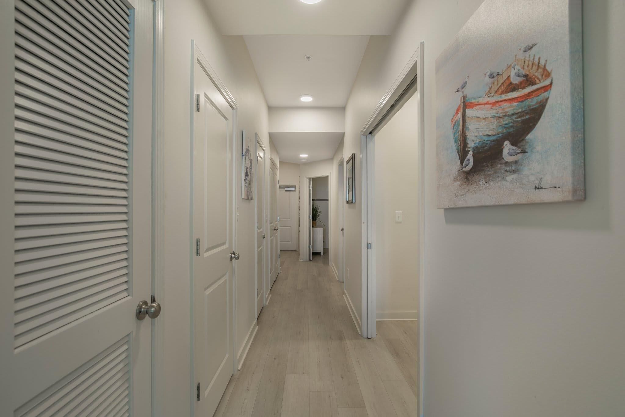 A hallway with white doors, a painting of a boat, and a ceiling light.