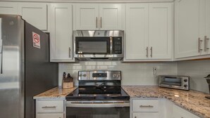 A kitchen with white cabinets, a stainless steel refrigerator, a microwave, an oven, a toaster, and a knife block. - Sea Glass 304 (Gulf Shores)
