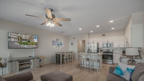 A spacious living room with a ceiling fan, a dining area with a table and chairs, a kitchen with modern appliances, and a large window with a view of a building. - Sea Glass 304 (Gulf Shores)