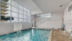 An indoor swimming pool with clear glass walls, a brick floor, and a staircase leading to upper levels. - Crystal Shores W 301 (Gulf Shores)