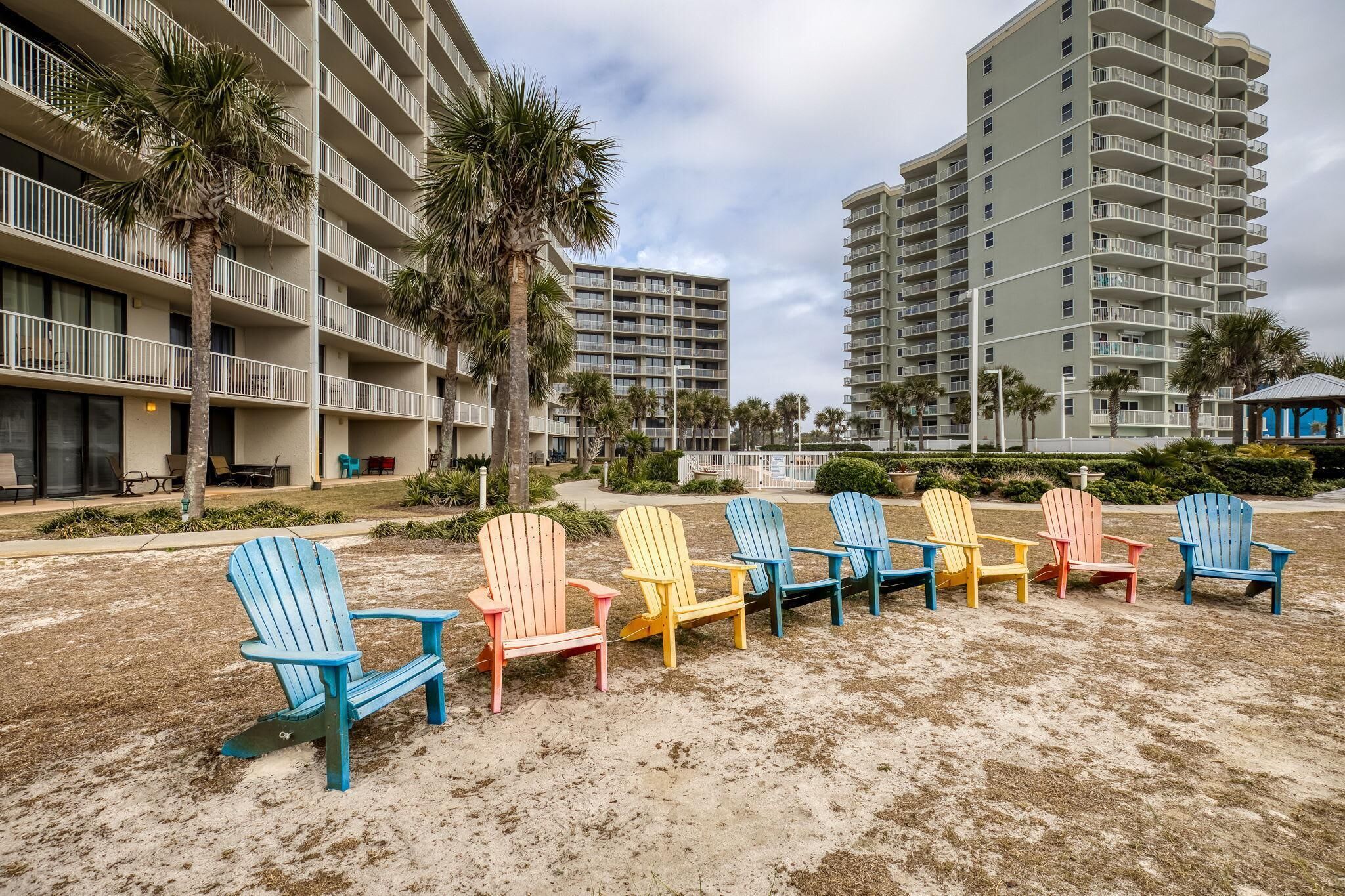 Un hôtel en bord de mer, composé de plusieurs bâtiments à étages, doté d’un espace extérieur avec des chaises Adirondack colorées et de palmiers.