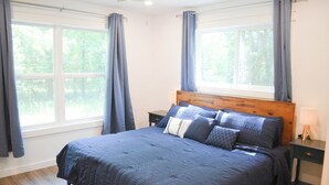 Un dormitorio con una cama grande, cabecera de madera, dos mesitas de noche y una ventana con cortinas.
