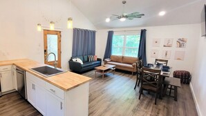 Una cocina moderna con horno empotrado y encimera de madera. Hay un comedor con mesa y sillas, y un sofá.