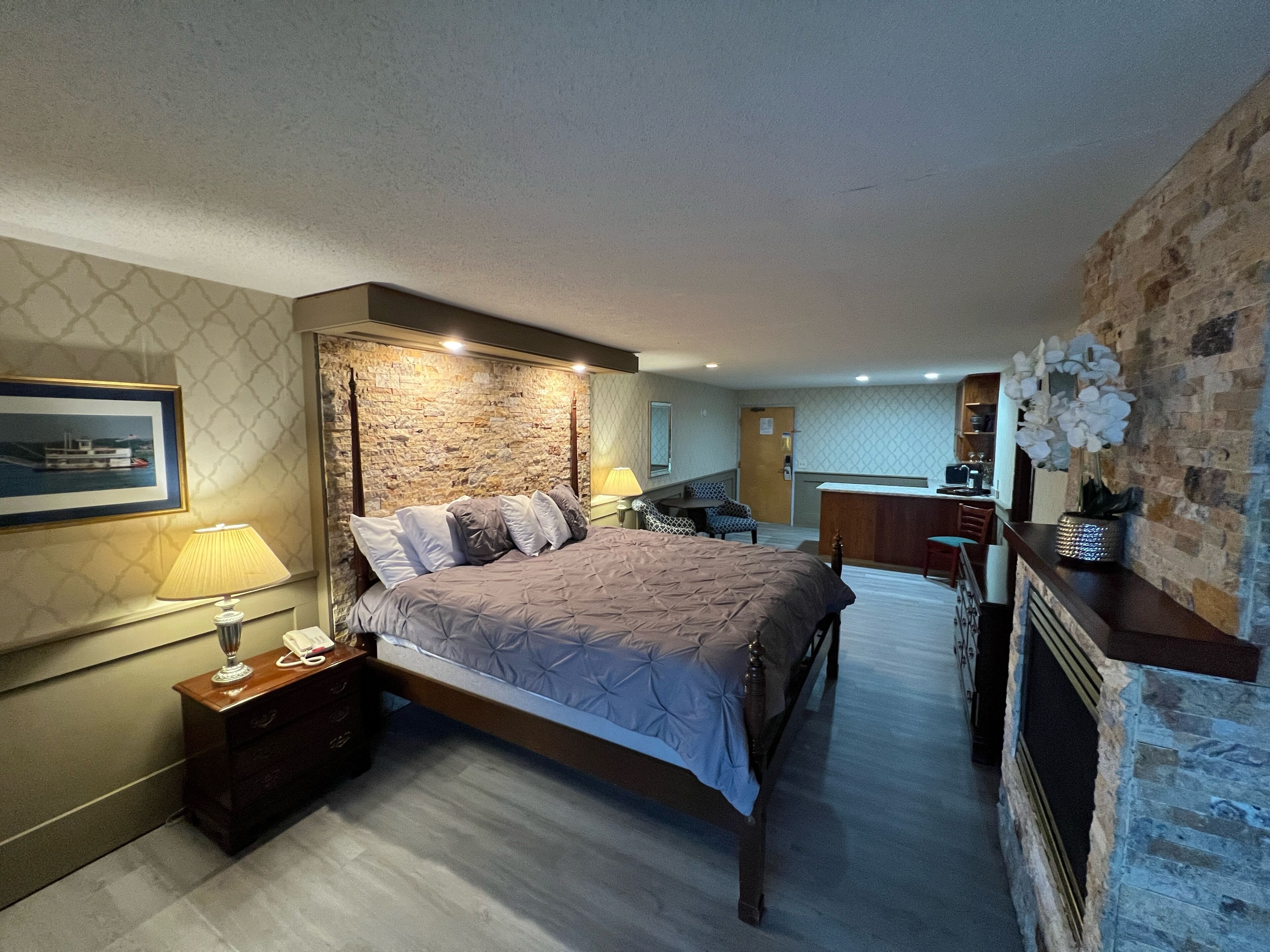 A bedroom with a stone wall, a bed, a nightstand, a desk, and a chair.