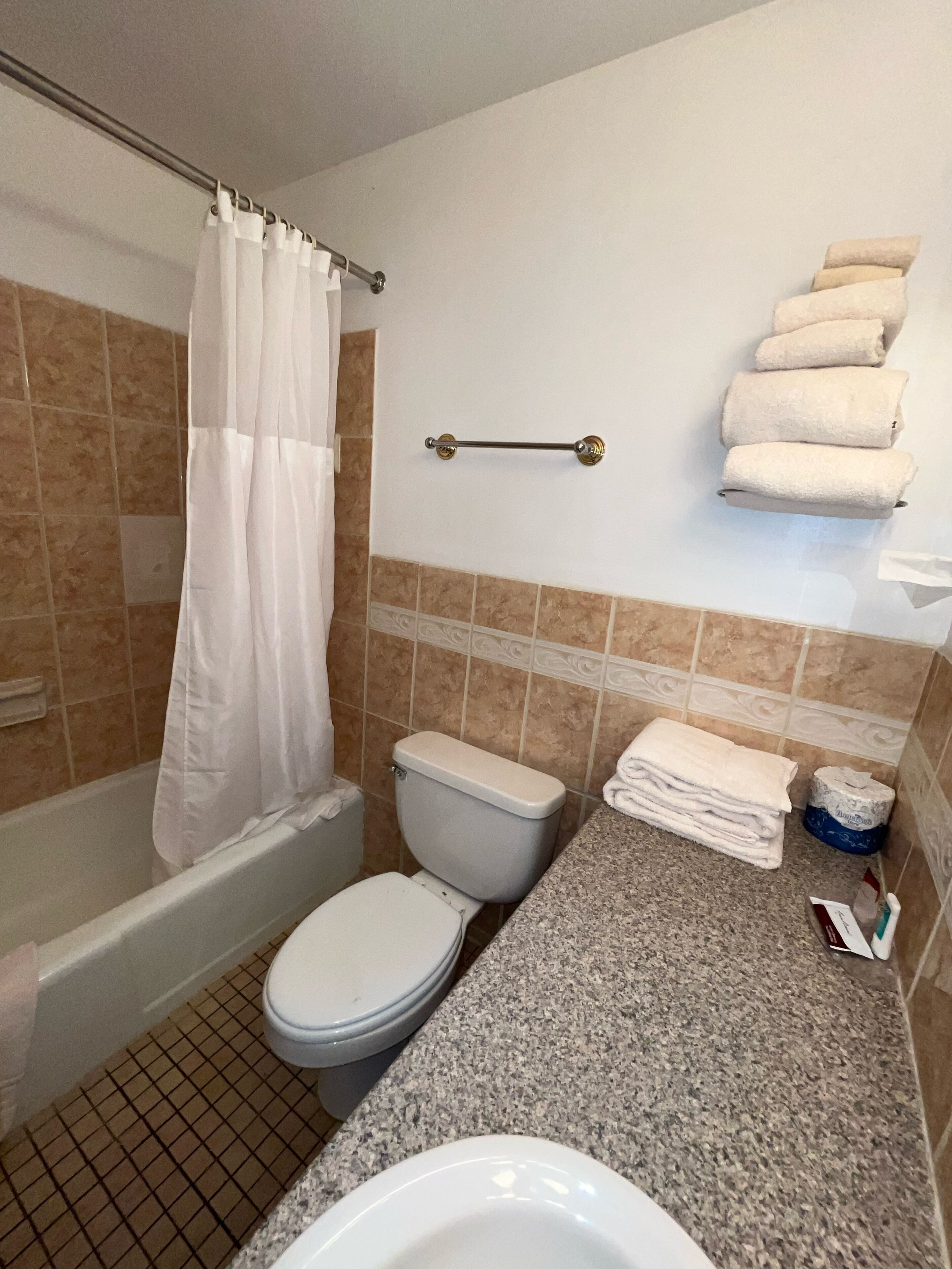 Un baño con inodoro, lavabo y bañera. Hay toallas apiladas en la pared y un rollo de papel higiénico en la encimera.