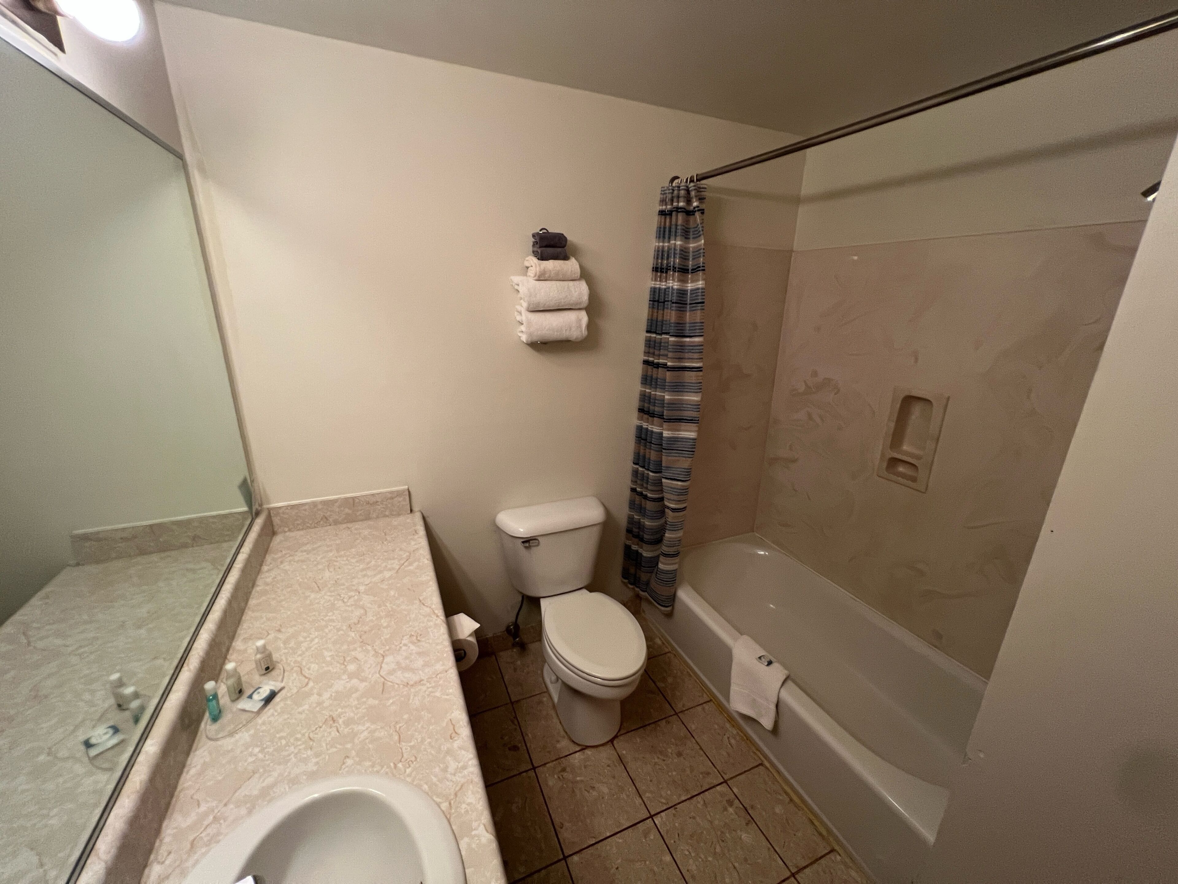 A bathroom with a toilet, a shower with a striped curtain, a sink with a mirror, and a bathtub.