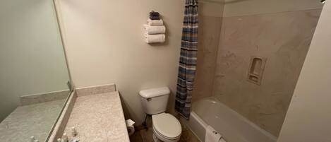 A bathroom with a toilet, a shower with a striped curtain, a sink with a mirror, and a bathtub.