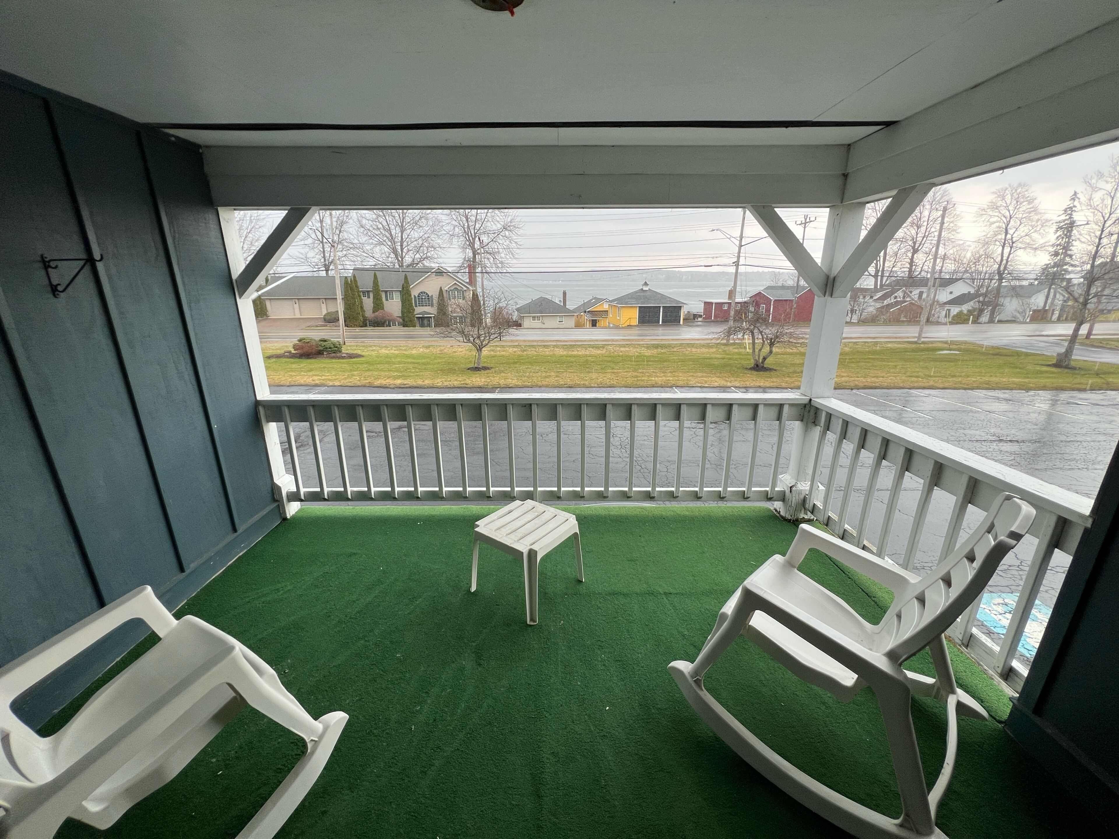 A covered porch with artificial green turf, two white rocking chairs, and a small table.