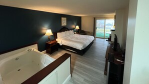 A hotel room with a large bed, a bathtub, a desk with a television, and a view of the outdoors. - Webb's Year Round Resort (Mayville)