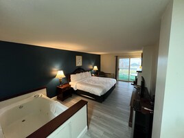 Habitación de hotel con una cama grande, una bañera, un escritorio con televisor y vistas al exterior.