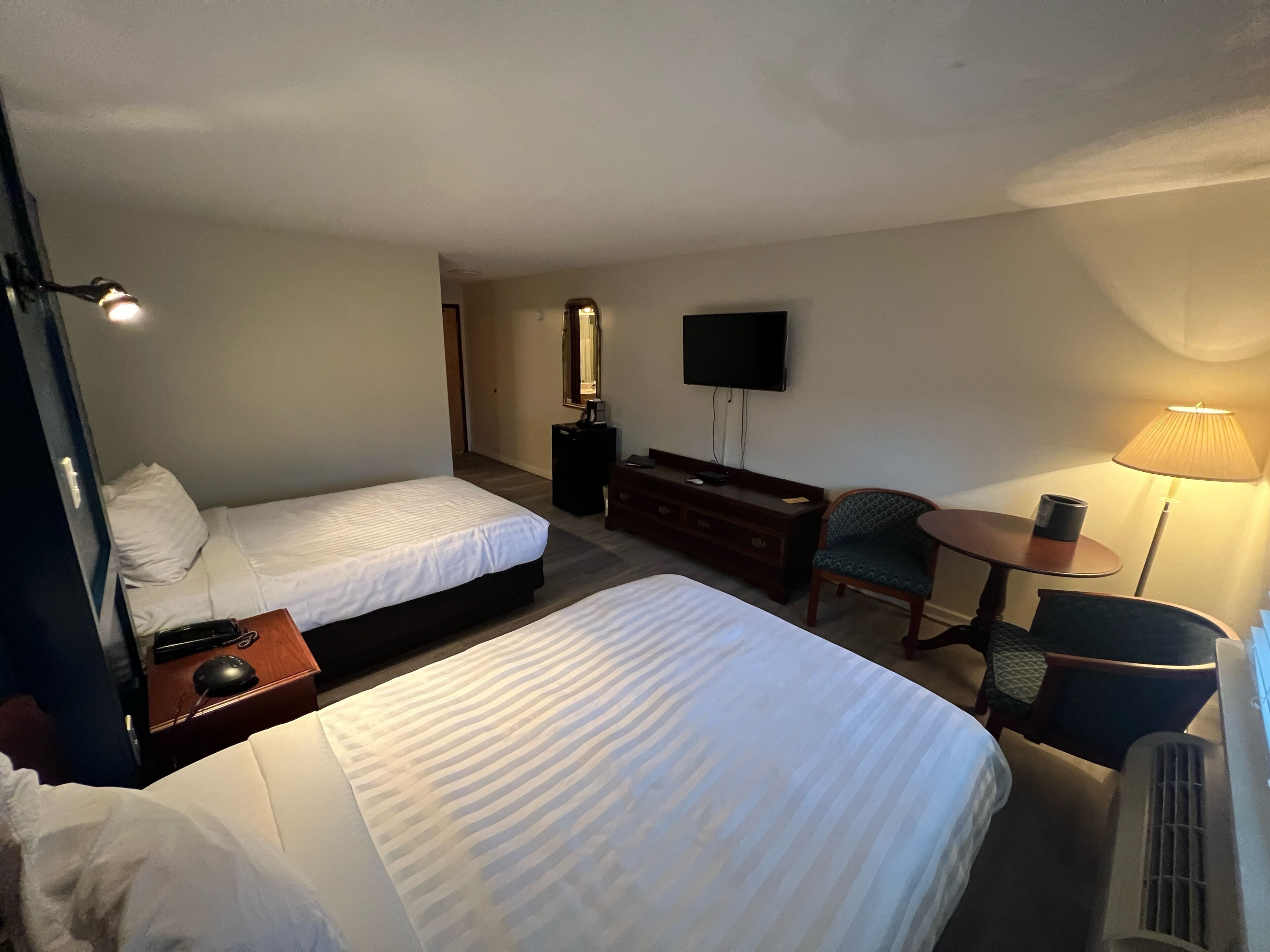 Et hotelværelse med to senge, et skrivebord med en computer, en stol, et fjernsyn og en lampe.