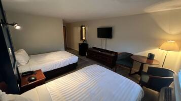A hotel room with two beds, a desk with a computer, a chair, a TV, and a lamp.