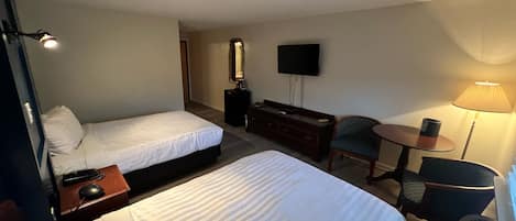 Et hotelværelse med to senge, et skrivebord med en computer, en stol, et fjernsyn og en lampe.