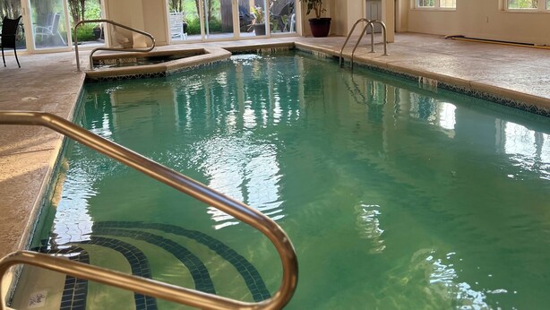 An indoor swimming pool with clear water, a 3-foot depth marking, and a view of the outside through large windows. - Webb's Year Round Resort (Mayville)