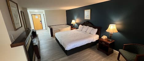 Habitación de hotel con una cama grande, lámparas de noche, una silla, un escritorio y vista al pasillo.