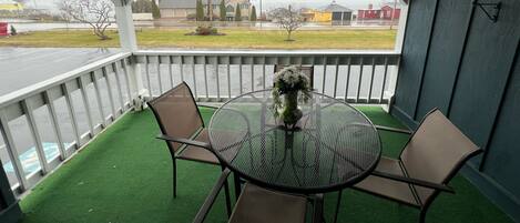 A covered outdoor seating area with a round table and four chairs, a potted plant, and a view of a residential street.