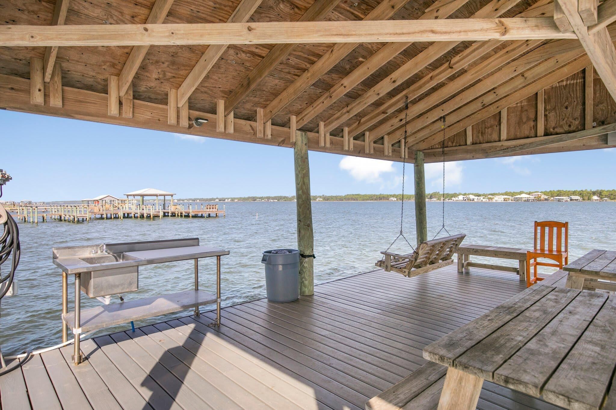 A wooden deck with a bench, a table, and a hanging chair overlooking a body of water.