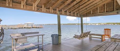 A wooden deck with a bench, a table, and a hanging chair overlooking a body of water.