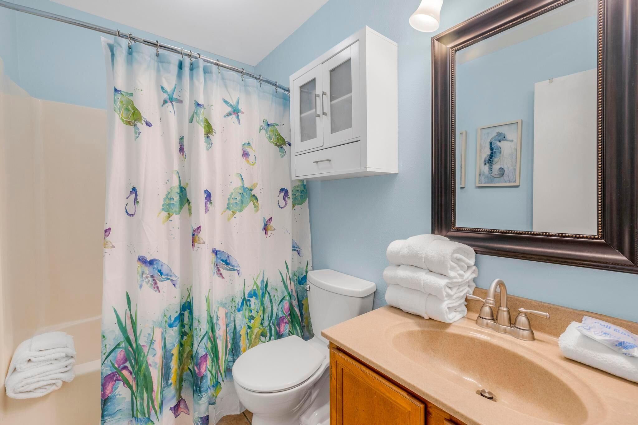 A bathroom with a shower curtain featuring aquatic designs, a toilet, a sink with a mirror, and a cabinet above the sink.