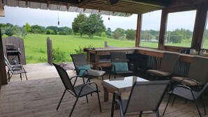 Eine Terrasse im Freien mit Holzboden, Metallstühlen, einem Tisch und einem Grillbereich.