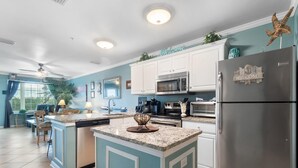 A modern kitchen with a central island, stainless steel appliances, and teal cabinetry. - Grand Caribbean 115 (Orange Beach)
