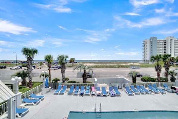 A rooftop pool area with blue lounge chairs and a view of the beach and ocean.