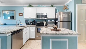 A kitchen with white cabinets, a microwave, a stove, a dishwasher, and a refrigerator. - Grand Caribbean 115 (Orange Beach)