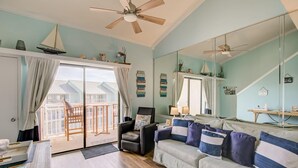 Un salon avec un canapé, un fauteuil et une table à manger. Il y a un balcon qui offre une vue sur les maisons.