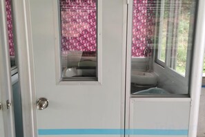 Une salle de bain avec des toilettes et un lavabo, une fenêtre donnant sur un paysage agréable et une porte avec une poignée.