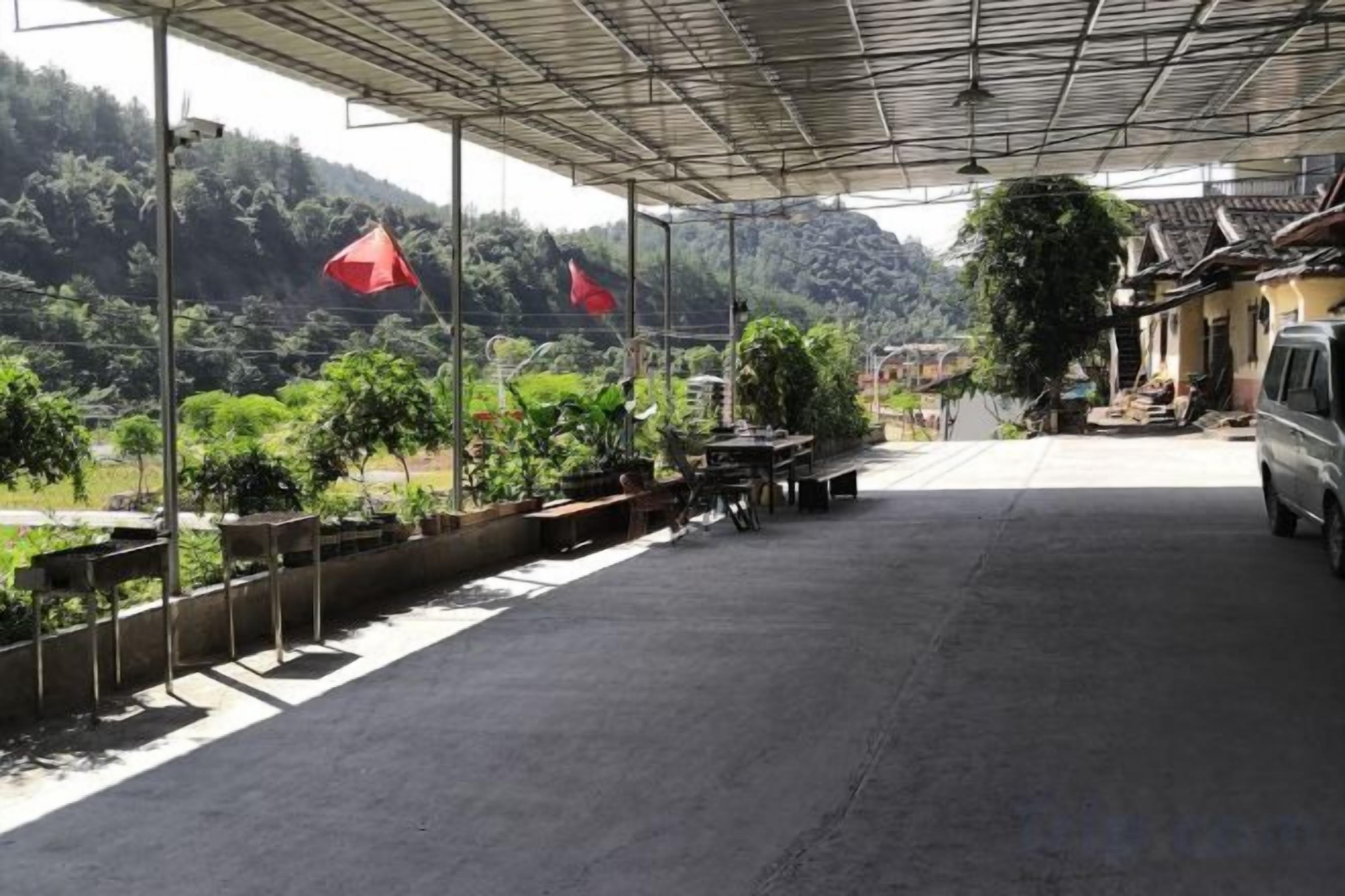 Uma área externa coberta com piso pavimentado, plantas em vasos e um veículo estacionado.