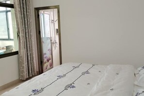 A bedroom with a bed, a window with curtains, and a door with a mirror.