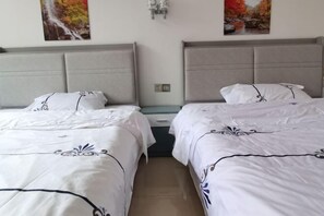 Une chambre d’hôtel avec deux lits, chacun agrémenté de draps blancs et de motifs décoratifs. Des appliques murales éclairent la pièce, et deux tableaux encadrés sont accrochés au-dessus des lits.