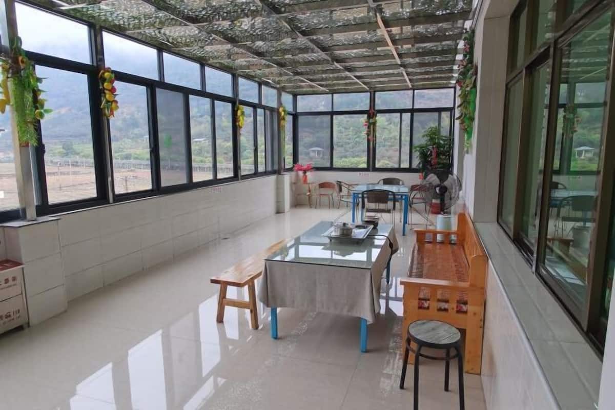 Une pièce spacieuse avec une table en verre et des bancs, de grandes fenêtres donnant sur l’extérieur et un plafond orné d’un motif texturé original.