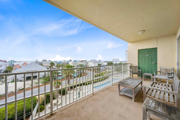 A balcony with a view of a beach, a green door, and wooden furniture. - The Indies 303 (Gulf Shores)