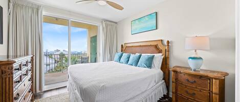 A bedroom with a bed, a dresser, a nightstand, a ceiling fan, a window with curtains, and a painting on the wall.