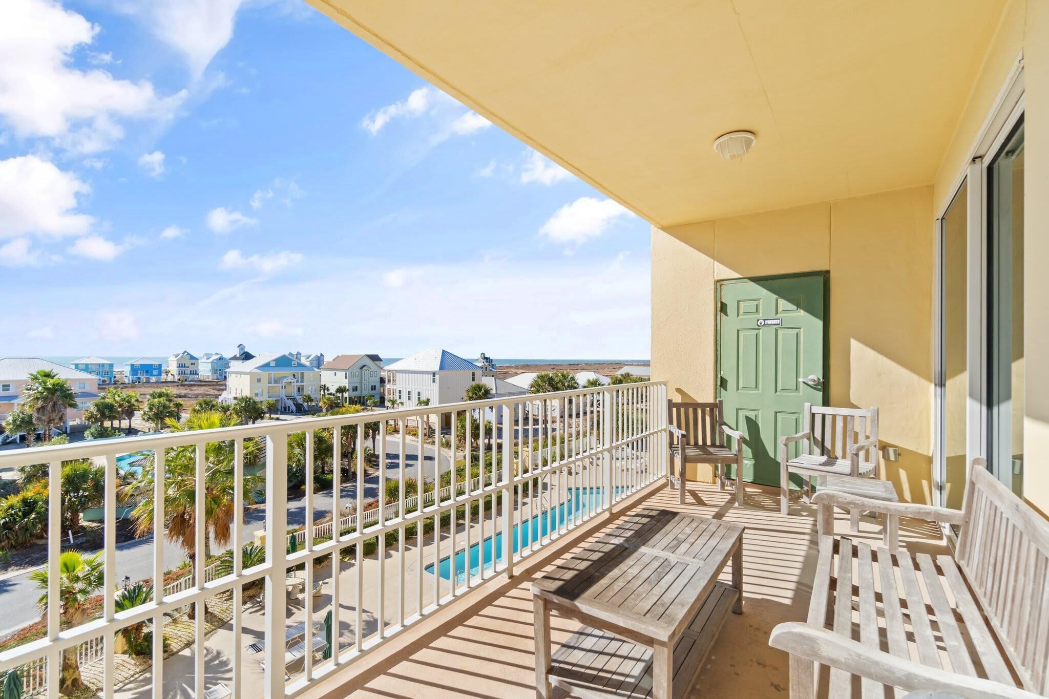 A balcony with a view of a swimming pool, a green door, and a white railing.