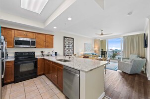 Una cocina moderna con microondas, horno y lavavajillas, una zona de comedor con vistas y un balcón con una silla.