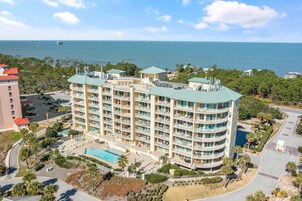 A multi-story hotel with a swimming pool, surrounded by greenery and a view of the sea.