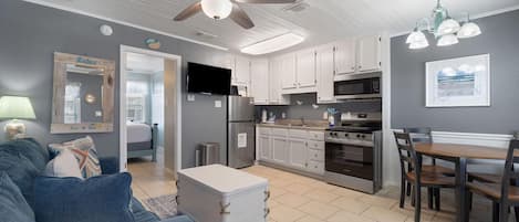Una cocina moderna con armarios blancos, un comedor con mesa y sillas de madera, un ventilador de techo y un televisor.