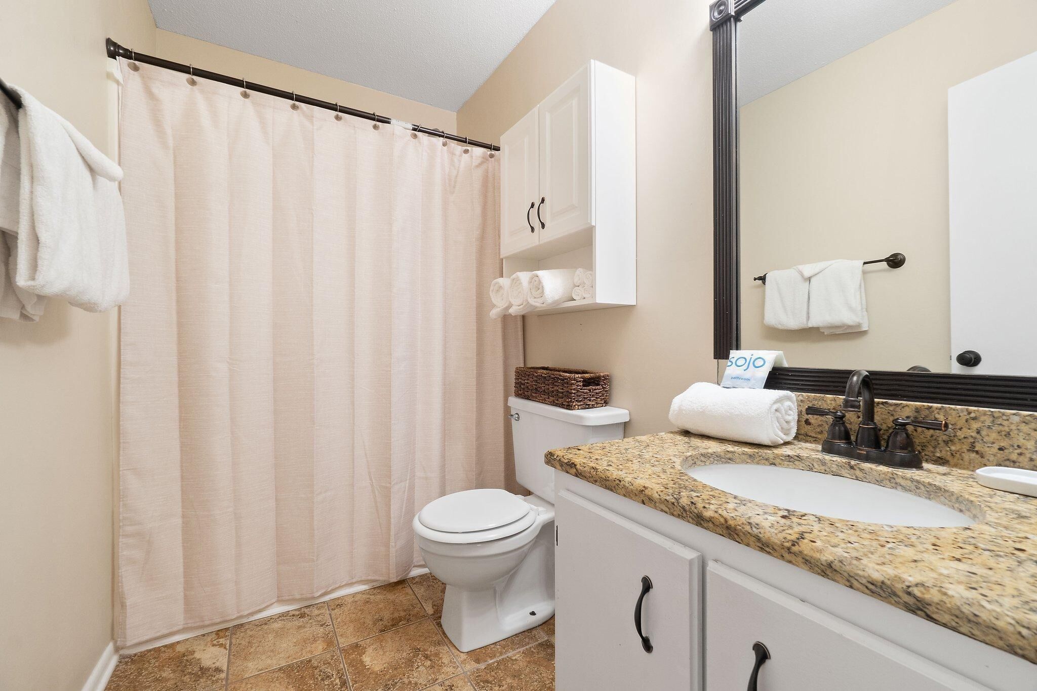 A bathroom with a shower curtain, toilet, sink, and a mirror.