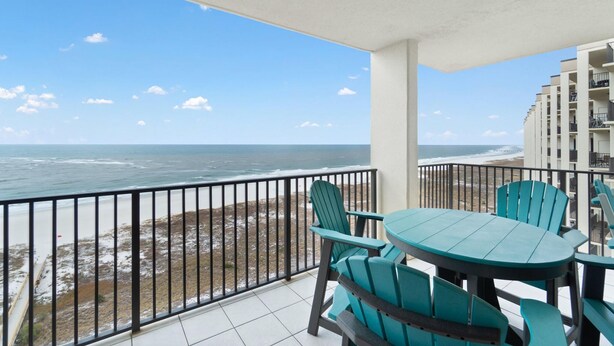 A balcony with a view of the ocean, a table with chairs, and a building in the background. - Phoenix Viii 81201 (Orange Beach)