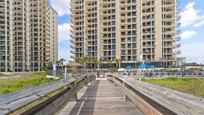 A wooden boardwalk leading to a beachfront area with high-rise buildings in the background. - Phoenix Viii 81201 (Orange Beach)
