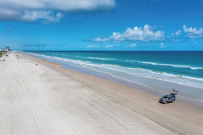 A beach with a sandy shore, a vehicle on the beach, and the ocean in the background.